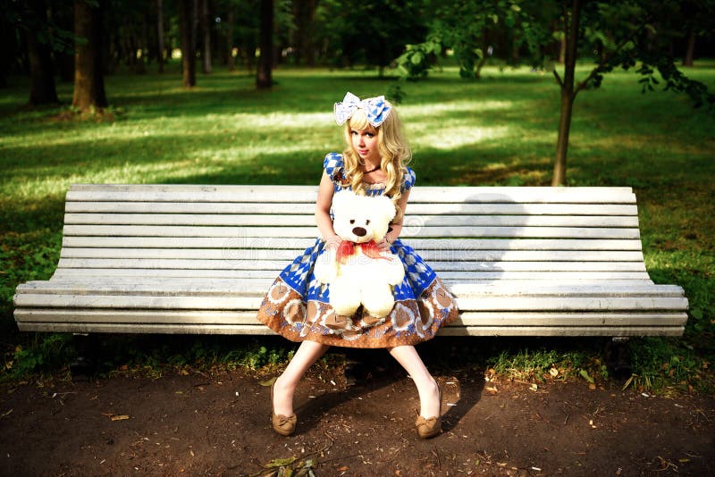 Portrait of young woman dressed as doll sitting on bench. Portrait of young woman dressed as doll sitting on bench.