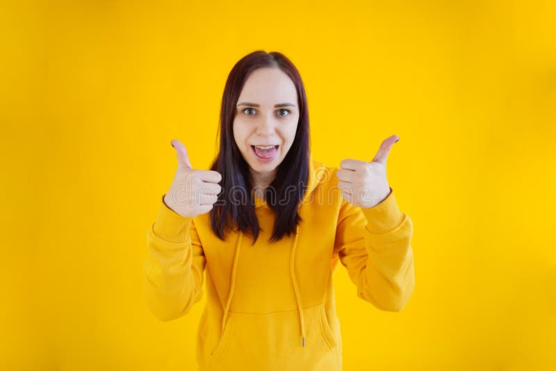Porträt der jungen Frau lächelnd und zeigt Daumen nach oben auf gelben Hintergrund. Nahaufnahme von glücklich brünette in gelb hoo lizenzfreies stockbild
