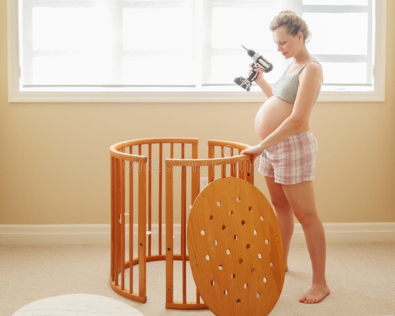 Porträt der jungen weißen kaukasischen glücklichen Frau, die zu Hause hölzerne Babykrippe in der Kindertagesstätte zusammenbaut stockfotos Porträt der jungen weißen kaukasischen glücklichen Frau, die zu Hause hölzerne Babykrippe in der Kindertagesstätte zusammenbaut stockfotos