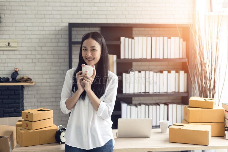 Porträt der lächelnden asiatischen jungen Frau mit dem Sparschwein und Pappschachteln, die im Haus stehen lizenzfreies stockfoto Porträt der lächelnden asiatischen jungen Frau mit dem Sparschwein und Pappschachteln, die im Haus stehen lizenzfreies stockfoto