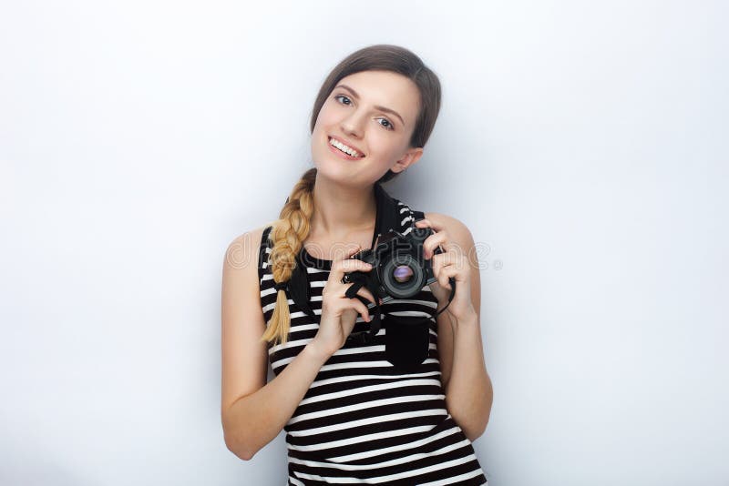 Porträt der lächelnden glücklichen jungen Schönheit im gestreiften Hemd, das mit schwarzer Fotokamera gegen Studiohintergrund auf lizenzfreie stockbilder Porträt der lächelnden glücklichen jungen Schönheit im gestreiften Hemd, das mit schwarzer Fotokamera gegen Studiohintergrund auf lizenzfreie stockbilder