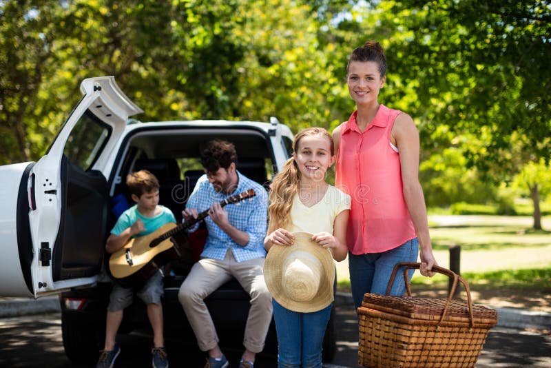 Porträt der Mutter und der Tochter, die mit Picknickkorb während Vater und Sohn spielen Gitarre in b steht lizenzfreie stockfotografie Porträt der Mutter und der Tochter, die mit Picknickkorb während Vater und Sohn spielen Gitarre in b steht lizenzfreie stockfotografie