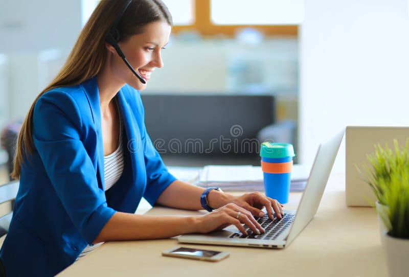Porträt der schönen Geschäftsfrau, die an ihrem Schreibtisch mit Kopfhörer und Laptop arbeitet stockbild