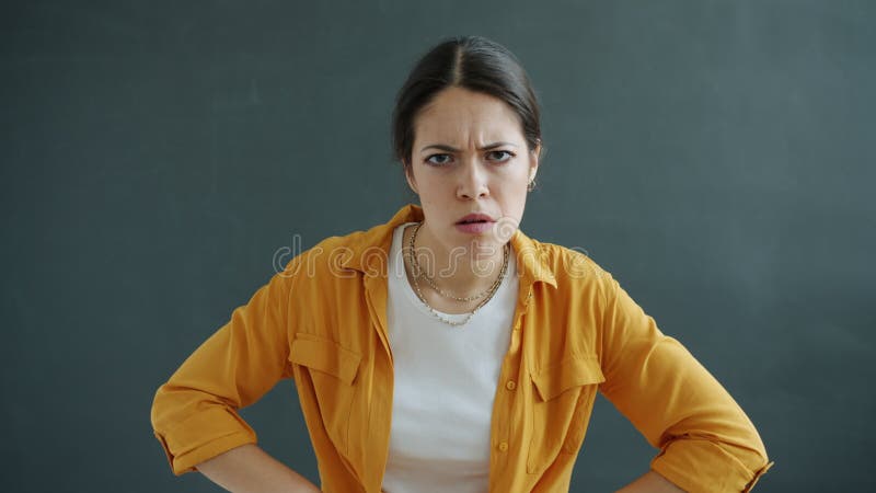 Porträt der Unglücklichen und der wütenden jungen Frau, welche die Kamera steht in die Seite gestemmt auf grauem Hintergrund betra