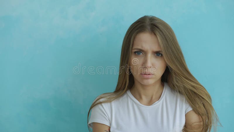 Porträt der verärgerten jungen Frau, die die Kamera nervös auf blauem Hintergrund untersucht