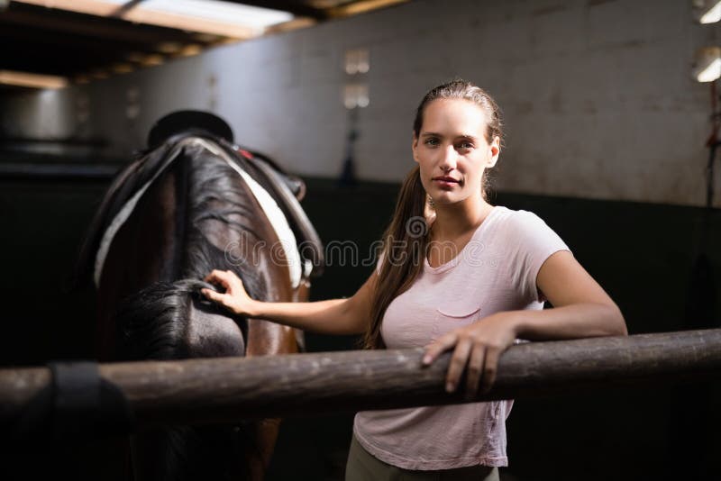 Porträt des bereitstehenden Pferds des jungen weiblichen Jockeys lizenzfreies stockbild Porträt des bereitstehenden Pferds des jungen weiblichen Jockeys lizenzfreies stockbild