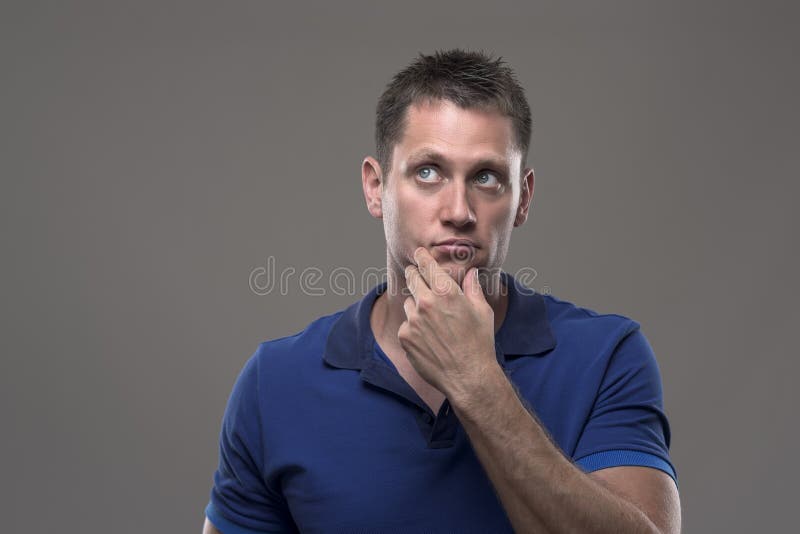 Porträt des durchdachten ernsten unsicheren jungen erwachsenen Mannes, der oben schaut, denkend mit der Hand auf Kinn stockfotografie