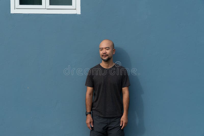 Porträt des düsteren Mannes Bartes Vierzigern Asiens im Gelegenheitsarbeit Tuch auf dem blauen Wandhintergrund stockbild