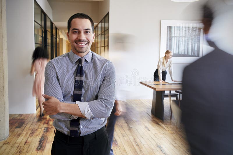 Porträt des jungen hispanischen Mannes an einem beschäftigten modernen Arbeitsplatz stockfoto