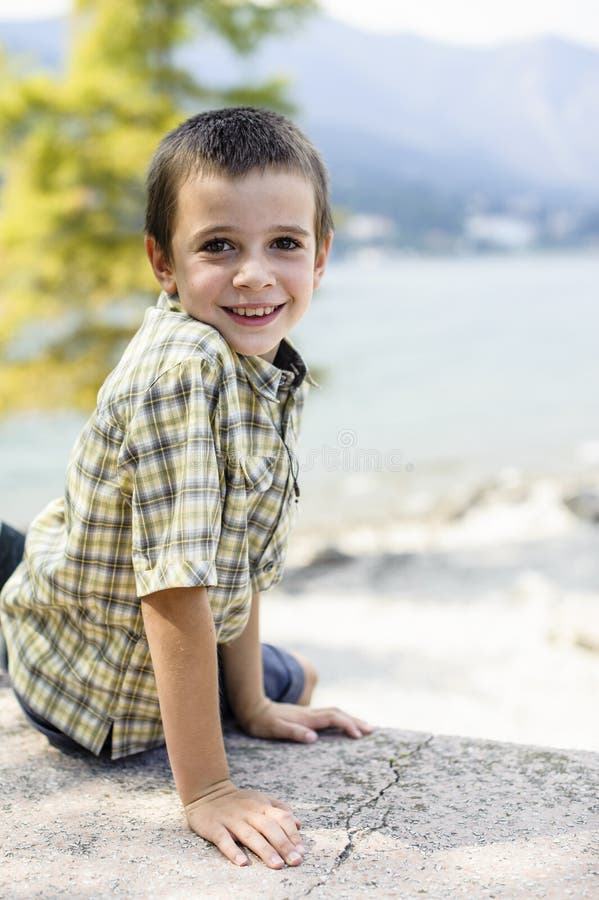Porträt des Jungen mit 9-Jährigen, der mit dem bunten Hemd sitzt O lächelt