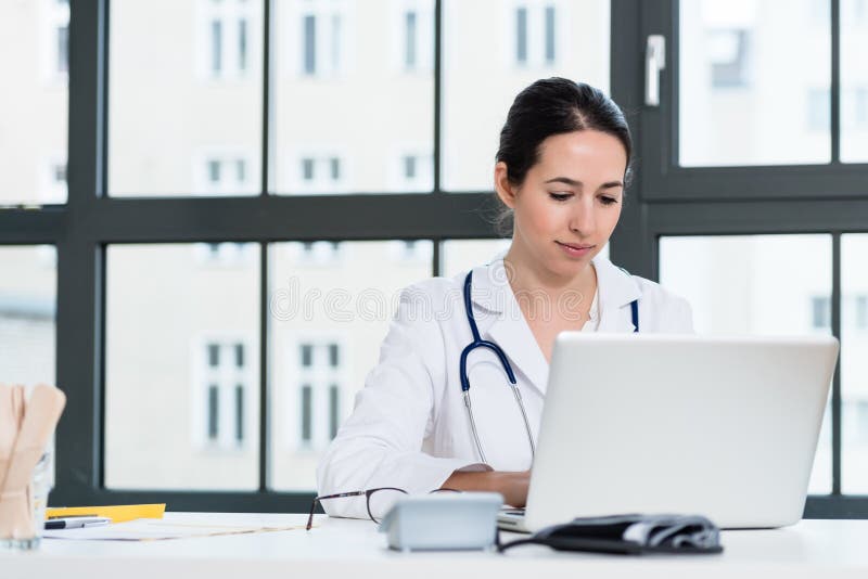 Porträt des jungen weiblichen Arztes, der an Laptop im Büro arbeitet