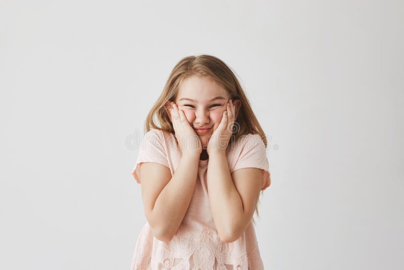 Porträt des lustigen blonden Mädchens im rosa Kleid, Gesicht mit den Händen zusammendrückend und machen die dummen Gesichter, die