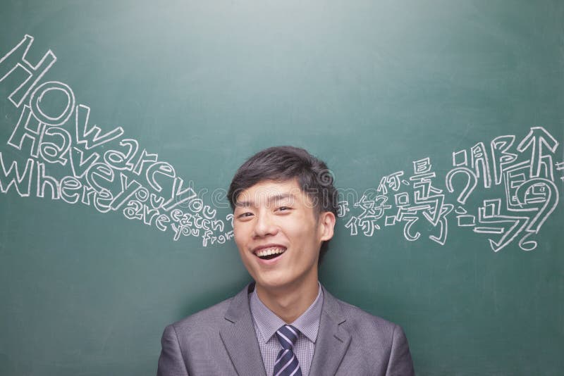 Portrait of smiling young businessman in front of black board with Chinese and English script coming from each ear. Portrait of smiling young businessman in front of black board with Chinese and English script coming from each ear