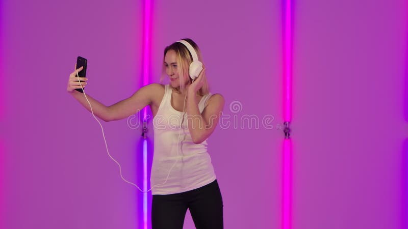 Porträt des modernen Modells genießen, tanzen und Musik in den großen weißen Kopfhörern mithilfe des Handys. junge Blondine stock footage
