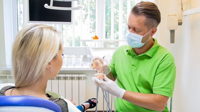 Porträt des männlichen Zahnarztes in der Schutzmaske sprechend mit seinem Patienten vor Behandlung lizenzfreies stockfoto Porträt des männlichen Zahnarztes in der Schutzmaske sprechend mit seinem Patienten vor Behandlung lizenzfreies stockfoto