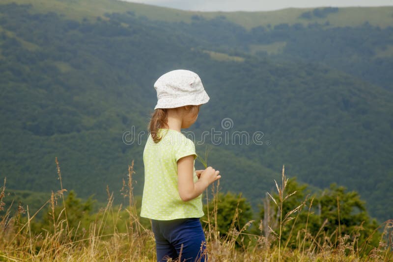 Porträt des netten kleinen Kindermädchens im Gras gegen Gebirgshintergrund. Frohe Kind haben einen Rest in den Bergen lizenzfreie stockfotos