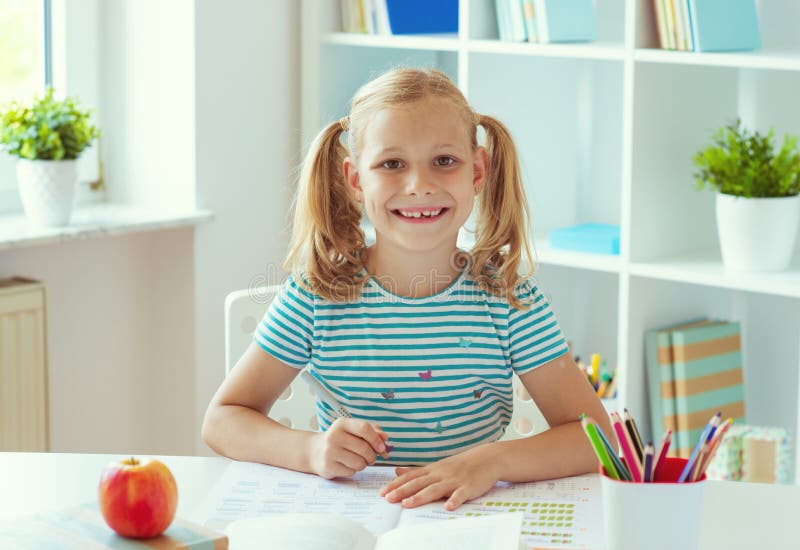 Porträt des netten Schulmädchens, das am weißen Tisch am hellen Klassenzimmer sitzt lizenzfreie stockbilder Porträt des netten Schulmädchens, das am weißen Tisch am hellen Klassenzimmer sitzt lizenzfreie stockbilder