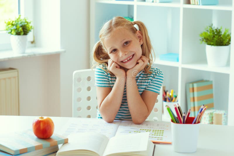 Porträt des netten Schulmädchens, das am weißen Tisch am hellen Klassenzimmer sitzt lizenzfreies stockfoto Porträt des netten Schulmädchens, das am weißen Tisch am hellen Klassenzimmer sitzt lizenzfreies stockfoto