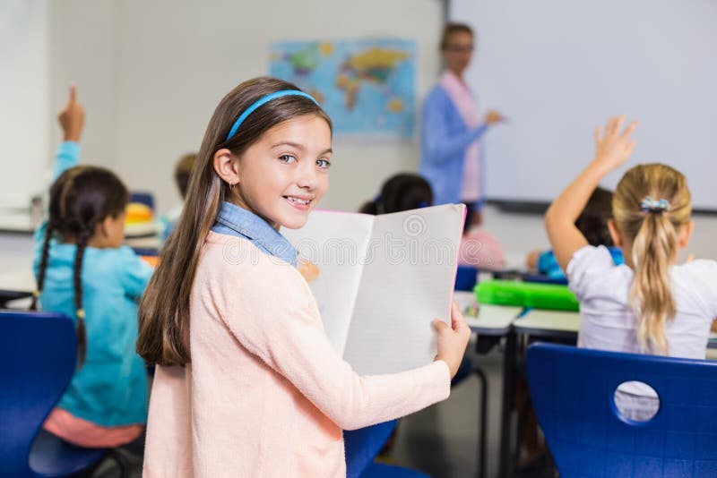 Porträt des Schulmädchens stehend mit Buch im Klassenzimmer