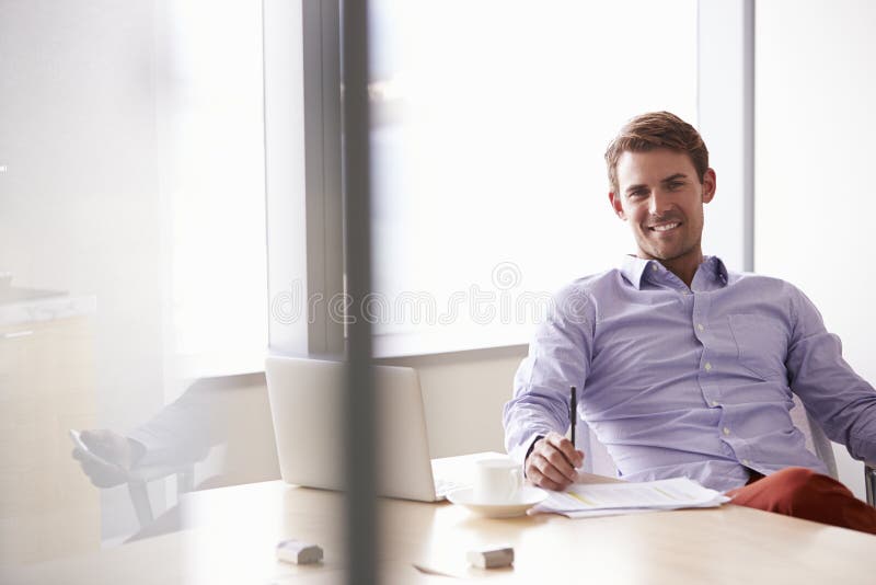 Portrait Of Casually Dressed Businessman Sitting At Desk. Portrait Of Casually Dressed Businessman Sitting At Desk