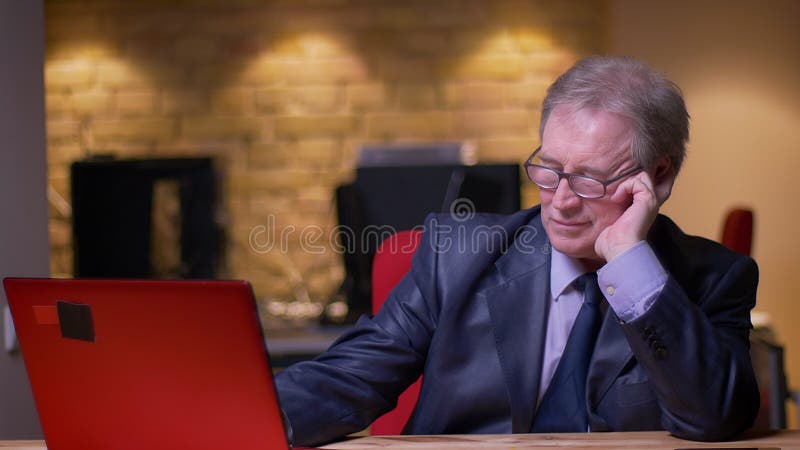 Porträt des älteren Geschäftsmannes im formalen Kostüm, das mit Laptop arbeitet, lehnt an Hand im Büro ermüdet sein