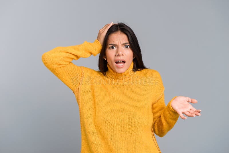 Portrait of a confused young woman dressed in sweater standing isolated over grey background, shrugigng. Portrait of a confused young woman dressed in sweater standing isolated over grey background, shrugigng