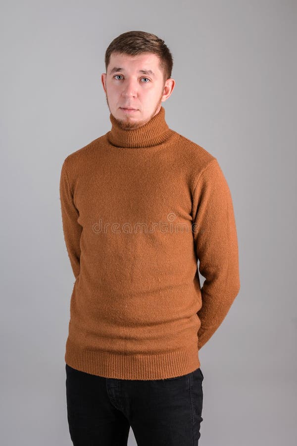 Porträt eines bärtigen Mannes, der in einem roten Pullover steht, mit seinen Händen hinter seinem Rücken auf grauem Hintergrund lizenzfreie stockfotos