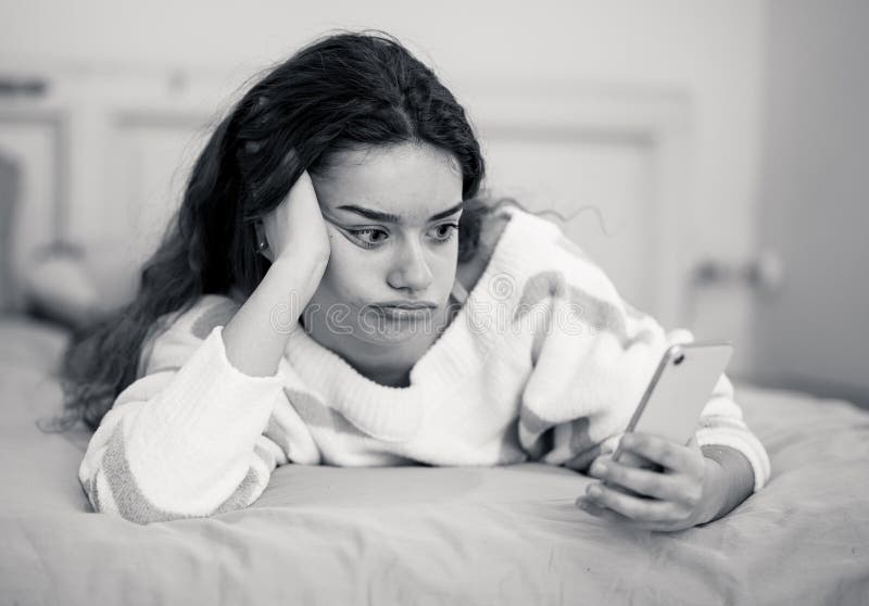 Porträt eines gebohrten, unglücklichen und müden hübschen jungen Mädchens unter Verwendung des Handys im Bett lizenzfreies stockbild Porträt eines gebohrten, unglücklichen und müden hübschen jungen Mädchens unter Verwendung des Handys im Bett lizenzfreies stockbild