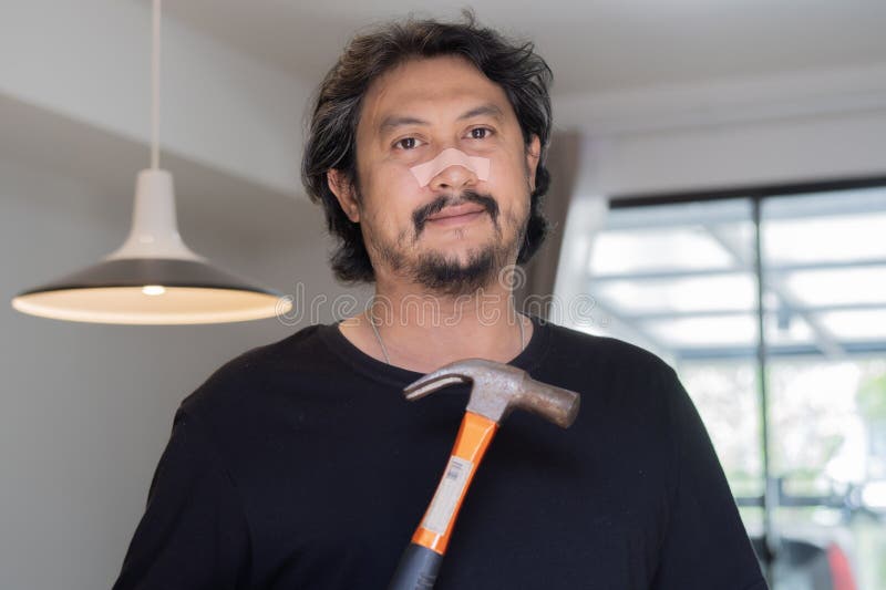 Portrait of happy Asain handsome man holding a silver claw hammer at home. Home repair work concept. Portrait of happy Asain handsome man holding a silver claw hammer at home. Home repair work concept