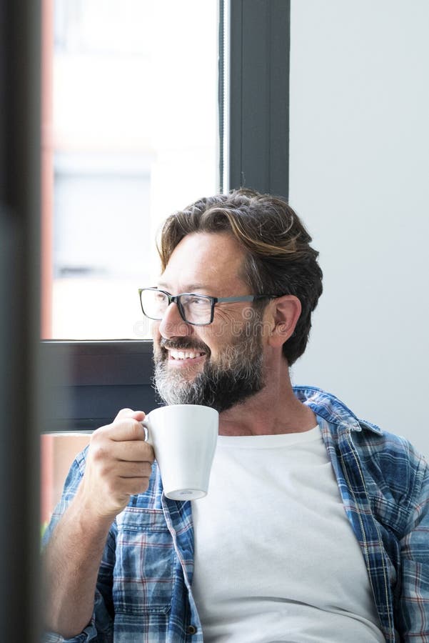 Porträt eines glücklichen Mannes, der aus dem Fenster schaute und zu Hause einen Kaffee trinken lächelnd, kaukasischen Mann mit Ba lizenzfreie stockfotografie
