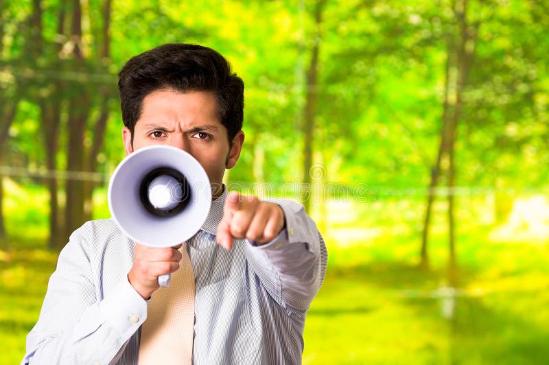 Porträt eines gutaussehenden Mannes, der mit einem Megaphon schreit, während er vor ihm seine Hand zeigt, in einem unscharfen Grü lizenzfreie stockfotografie Porträt eines gutaussehenden Mannes, der mit einem Megaphon schreit, während er vor ihm seine Hand zeigt, in einem unscharfen Grü lizenzfreie stockfotografie