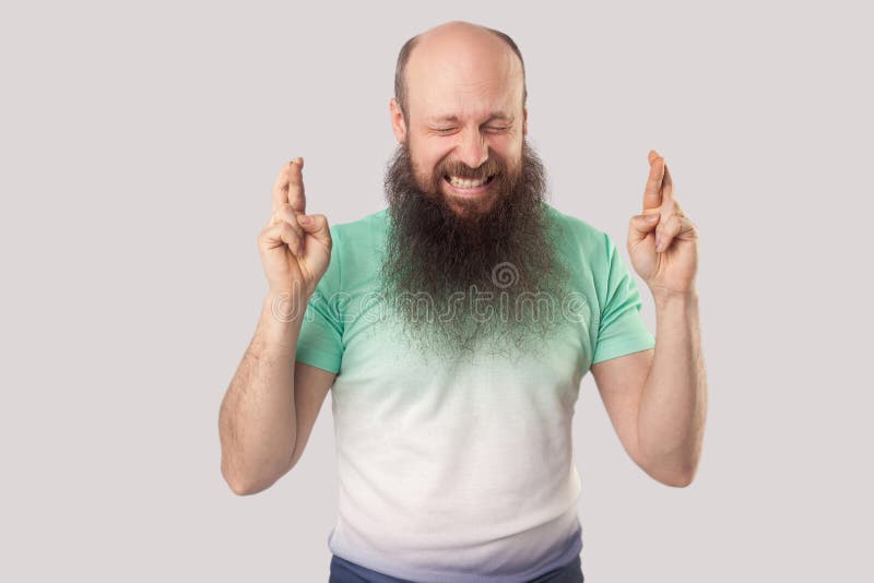 Porträt eines hoffnungsvollen Glatzbärtenmänners mittleren Alters in grünem T-Shirt-Stehen, gekreuzten Fingern, Zähne, geschlosse