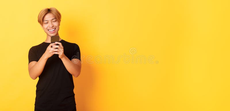 Porträt eines hübschen, stylischen Asiaten mit blonden Haaren, der Mobiltelefon benutzt und in der Smartphone-App lächelnde Nachri lizenzfreies stockfoto