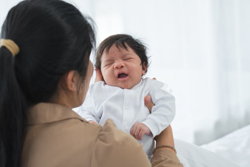 Porträt eines mehrrassigen Neugeborenen, das weint oder gähnt oder in Arm einer asiatischen Mutter liegt. Kleine süße Kindesausdrü lizenzfreie stockfotos