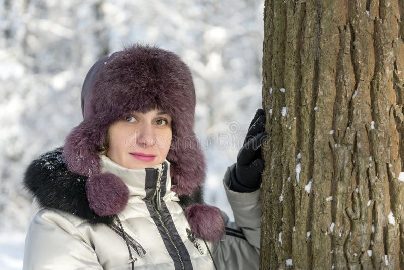 Porträt eines Mädchens in einer Jacke und in einem Hut in einem Wald nahe einem Baum Tag, Winter lizenzfreie stockfotos