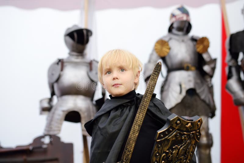 Porträt eines netten kleinen Jungen gekleidet als mittelalterlicher Ritter mit einer Klinge und einem Schild auf Hintergrund der stockfotografie Porträt eines netten kleinen Jungen gekleidet als mittelalterlicher Ritter mit einer Klinge und einem Schild auf Hintergrund der stockfotografie