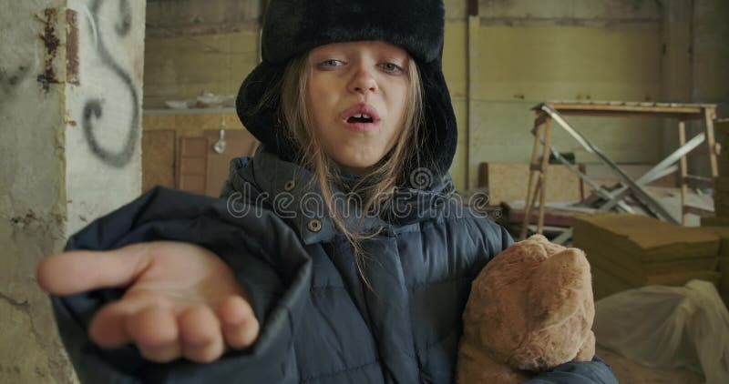 Porträt eines obdachlosen kaukasischen Mädchens in schmutzigen Winterbekleidung, das den Teddybären hält und um ein Aushängeschil