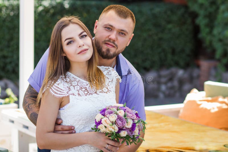 Porträt eines romantischen Paares gegen einen Hintergrund von grünen Büschen und von Bäumen, Mädchen, das Blumen in den Händen, j lizenzfreie stockbilder Porträt eines romantischen Paares gegen einen Hintergrund von grünen Büschen und von Bäumen, Mädchen, das Blumen in den Händen, j lizenzfreie stockbilder
