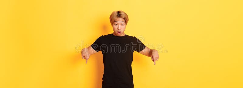 Porträt eines überraschten asiatischen Jungs, der erstaunliche Zeigefinger schnappt und auf einen gelben Hintergrund mit Banner sc lizenzfreies stockbild