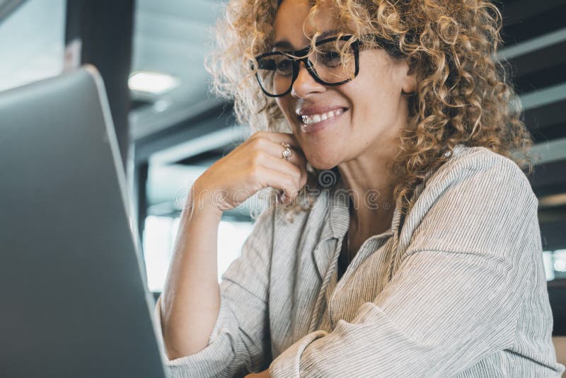 Porträt fröhlicher junger erwachsener Frau, die im Büro Latop benutzt. selbstbewusste Geschäftsfrau mit Brille lächelt am Computer stockbilder