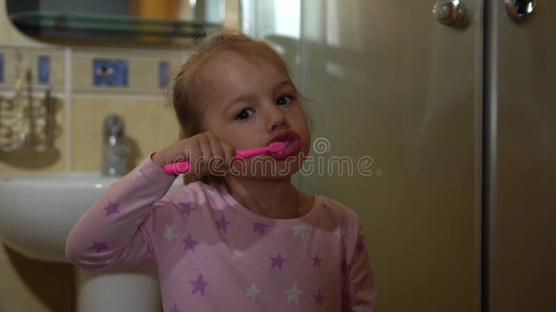 Porträt glücklich süß junge Vorschule Kind Mädchen auf Pyjama Zähneputzen und Blick auf die Kamera im Bad. Kindertageszeitung stock video