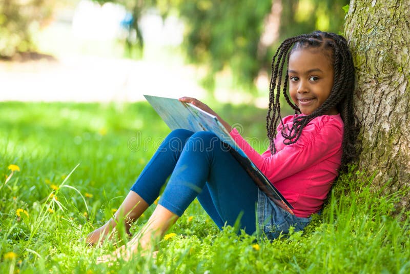 Porträt im Freien eines netten jungen schwarzen kleinen Mädchens, das einen Buh liest