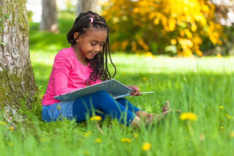 Porträt im Freien eines netten jungen schwarzen kleinen Mädchens, das einen Buh liest