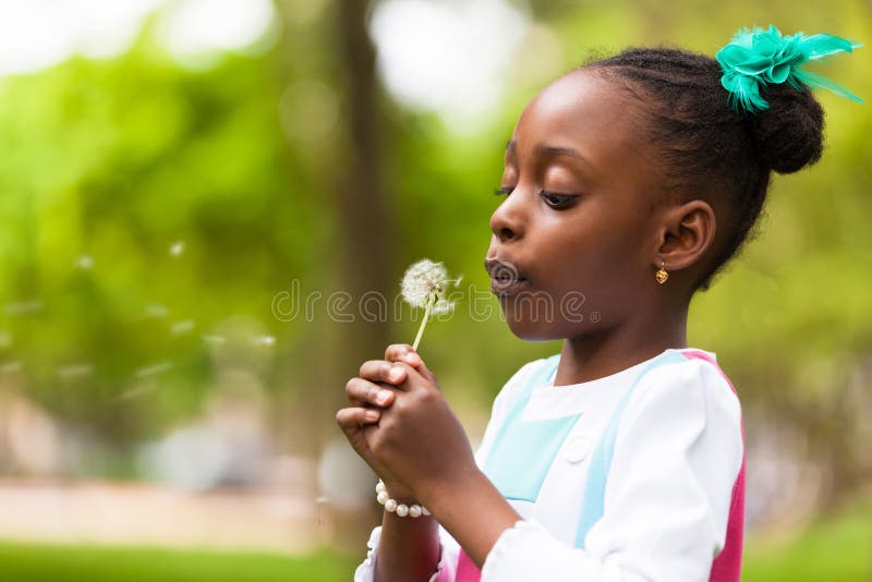 Porträt im Freien eines netten jungen schwarzen Mädchens, das einen Löwenzahn durchbrennt stockbild