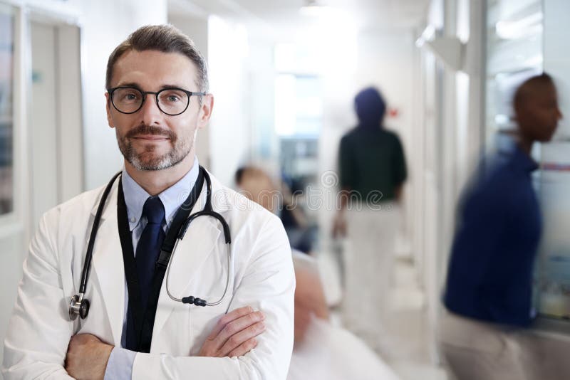 Porträt reifen männlichen Doktors Wearing White Coat mit Stethoskop im beschäftigten Krankenhaus-Korridor