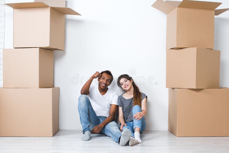 Porträt von den glücklichen jungen Paaren, die auf dem Boden betrachtet Kamera und träumt ihr neues Haus und Lieferung sitzen lizenzfreies stockbild Porträt von den glücklichen jungen Paaren, die auf dem Boden betrachtet Kamera und träumt ihr neues Haus und Lieferung sitzen lizenzfreies stockbild