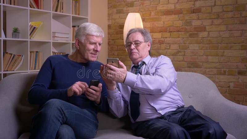 Porträt von den älteren männlichen Freunden, die miteinander Smartphones zeigen und froh lachen