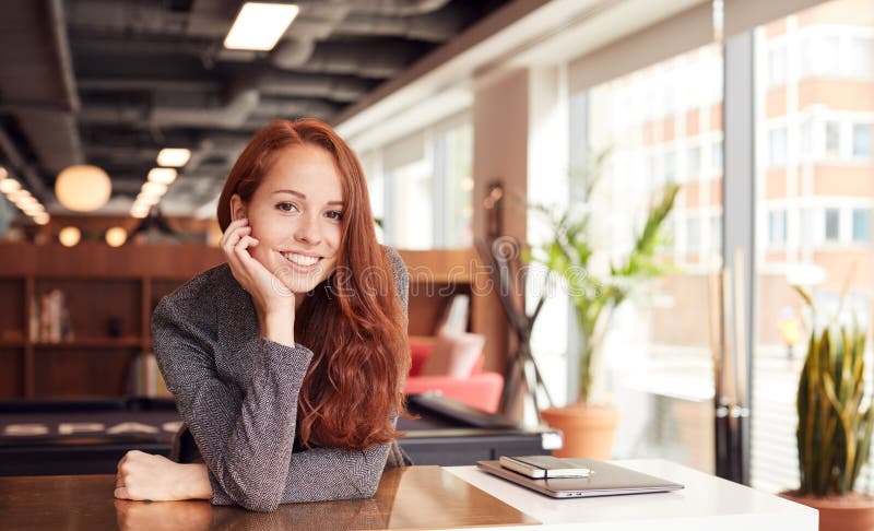 Portrait Of Casually Dressed Young Businesswoman Working At Desk In Modern Open Plan Workplace. Portrait Of Casually Dressed Young Businesswoman Working At Desk In Modern Open Plan Workplace