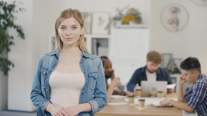 Porträt von jungen Blondinen Geschäftsfrau Blick in die Kamera und lächelnd im Büro Arbeitsplatz Hintergrund. der Begriff