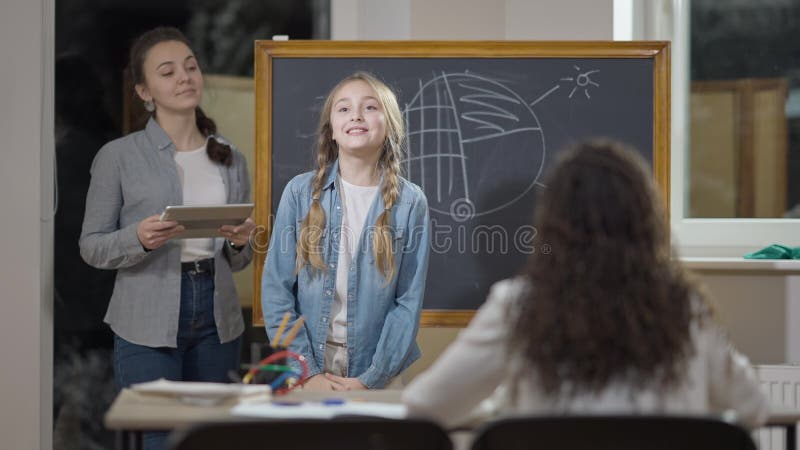 Porträt von smart cute kaukasischen Schulmädchen sprechen und lächeln im Klassenzimmer mit Lehrer und Klassenkamerad